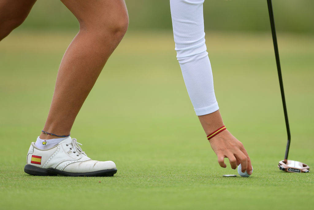 A marker being placed behind a golf ball on a green